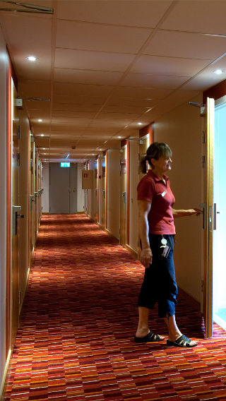 Μια γυναίκα στέκεται σε διάδρομο του Spar Hotel φωτισμένο με φωτισμό ξενοδοχείων της Philips