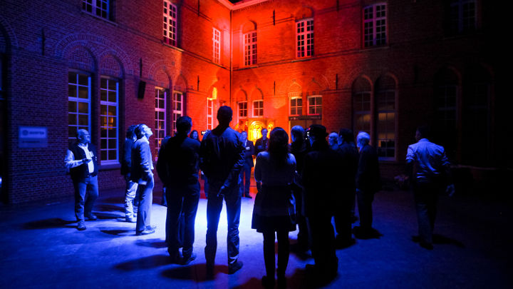 Μια μεγάλη ομάδα ανθρώπων συζητά στον εξωτερικό χώρο ενός όμορφα φωτισμένου κτιρίου στο Turnhout, Βέλγιο σε εργαστήριο που έχει οργανώσει η Philips