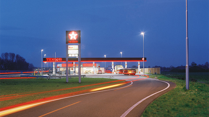 Ένα βενζινάδικο Texaco δίπλα στον αυτοκινητόδρομο, έντονα φωτισμένο το σούρουπο - εξωτερικός φωτισμός που τραβά την προσοχή