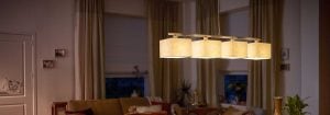 Μοντέρνο κρεμαστό φως LED με πολλαπλές αποχρώσεις υφασμάτων φωτίζει ένα άνετο σαλόνι, επιδεικνύοντας ενεργειακά αποδοτικές και κομψές λύσεις οικιακού φωτισμού για ατμοσφαιρική βραδινή άνεση.